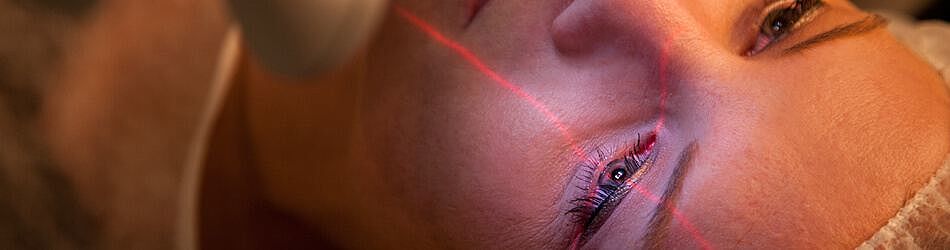 Frau lässt sich die Augen Lasern - der Laser markiert das linke Auge mit einem Fadenkreuz.